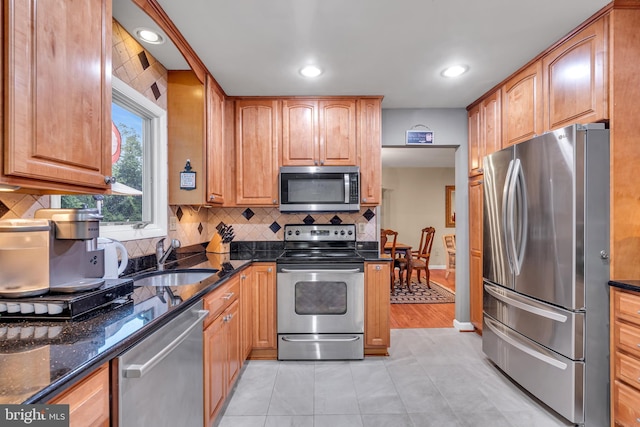 kitchen with appliances with stainless steel finishes, a sink, dark stone counters, decorative backsplash, and brown cabinets