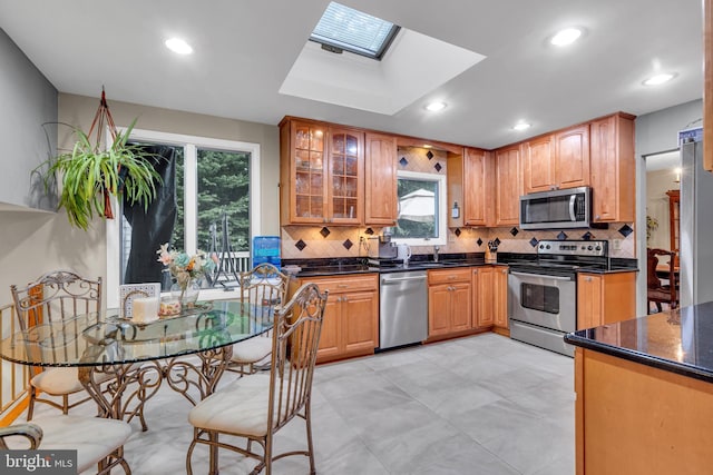 kitchen featuring stainless steel appliances, backsplash, glass insert cabinets, a skylight, and recessed lighting