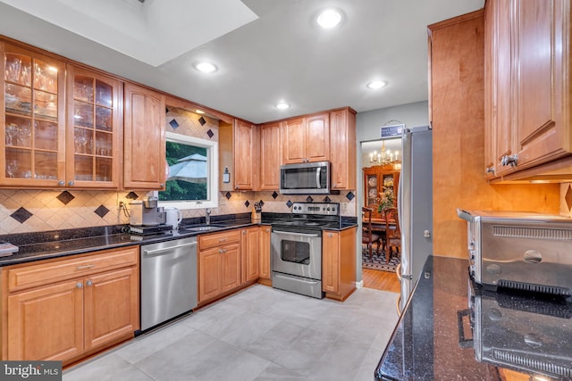kitchen with stainless steel appliances, glass insert cabinets, tasteful backsplash, dark stone countertops, and a sink