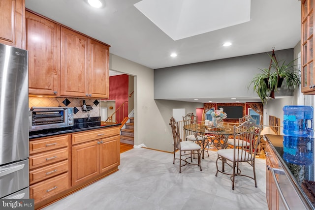 kitchen with freestanding refrigerator, recessed lighting, decorative backsplash, baseboards, and brown cabinets