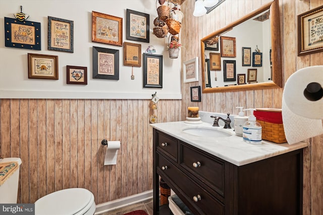 half bath with toilet, wainscoting, vanity, and wood walls