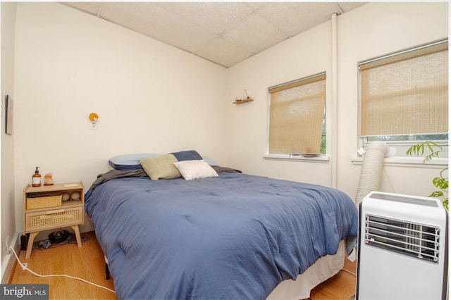 bedroom with wood finished floors, a paneled ceiling, and heating unit