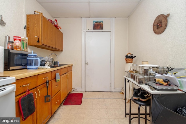 kitchen featuring light countertops, brown cabinetry, light flooring, stainless steel microwave, and a paneled ceiling