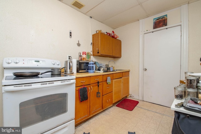 kitchen featuring electric stove, light countertops, brown cabinetry, a drop ceiling, and a sink