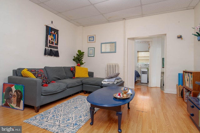 living area with radiator, a drop ceiling, and wood finished floors