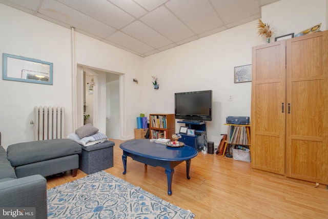living room featuring radiator heating unit, light wood-type flooring, and a drop ceiling