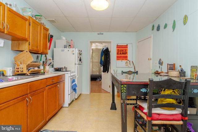 kitchen featuring white gas range oven, a drop ceiling, light countertops, and brown cabinets