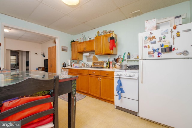 kitchen featuring white appliances, a paneled ceiling, light flooring, light countertops, and a sink