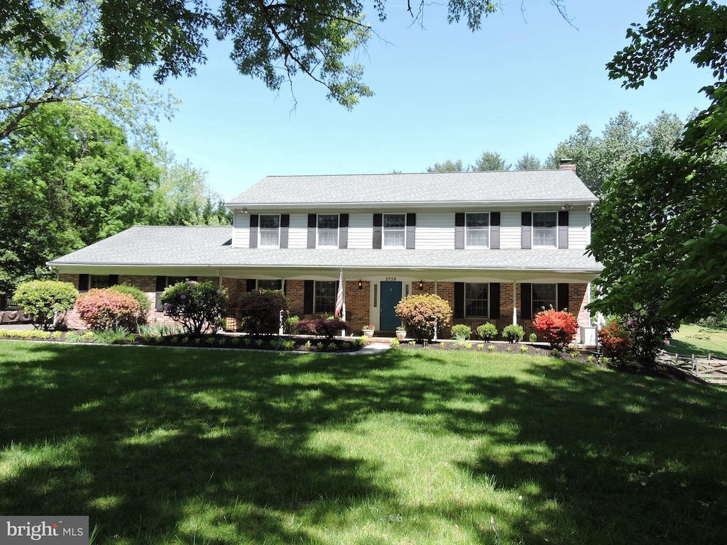 colonial home with a chimney, a front lawn, and brick siding