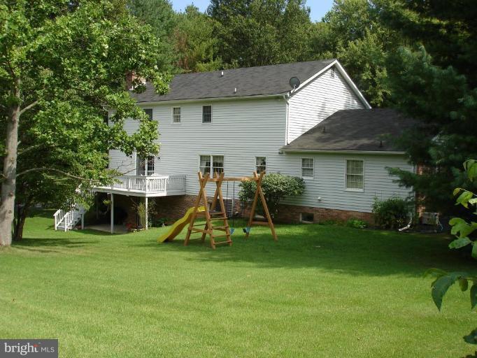 rear view of property with a playground, a yard, and a deck