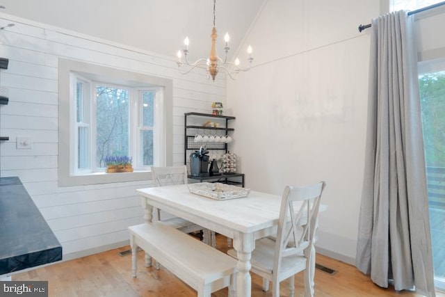 dining room featuring a chandelier, vaulted ceiling, light wood finished floors, and wooden walls