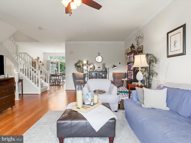 living area featuring stairs, wood finished floors, a ceiling fan, a chandelier, and ornamental molding