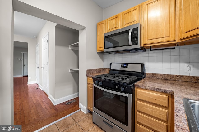kitchen featuring stainless steel appliances, decorative backsplash, baseboards, and dark countertops