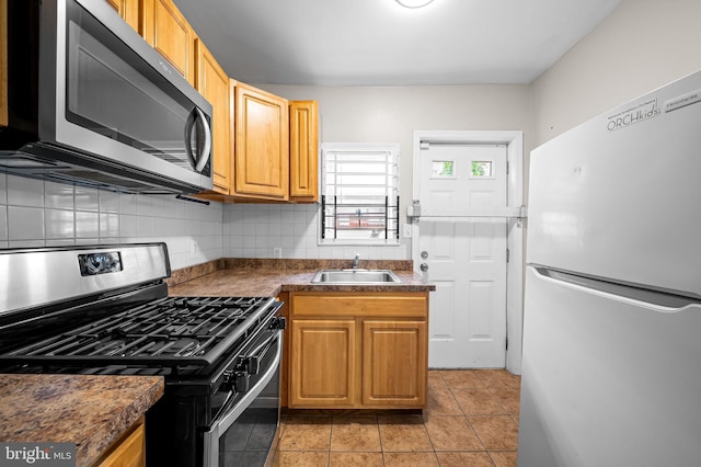 kitchen featuring stainless steel appliances, a sink, tasteful backsplash, dark countertops, and light tile patterned floors