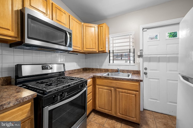 kitchen featuring appliances with stainless steel finishes, a sink, dark countertops, tasteful backsplash, and light tile patterned flooring