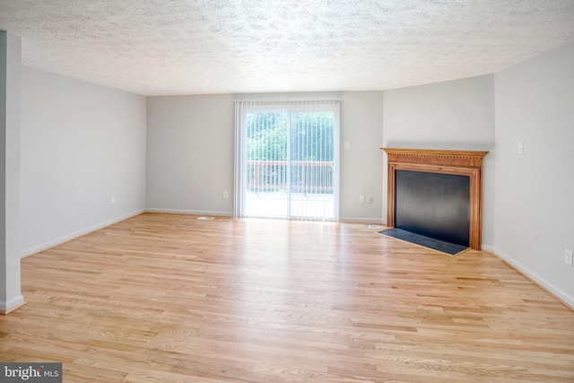 unfurnished living room featuring wood finished floors, a fireplace with flush hearth, a textured ceiling, and baseboards