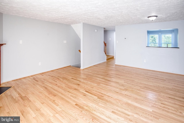 unfurnished living room with light wood-style flooring, stairs, a textured ceiling, and baseboards