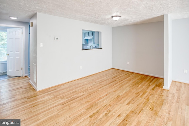 empty room featuring a textured ceiling, wood finished floors, and baseboards