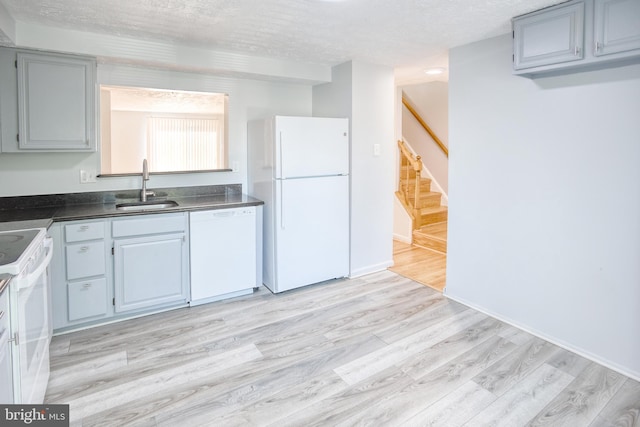 kitchen with a sink, white appliances, dark countertops, light wood-type flooring, and a textured ceiling