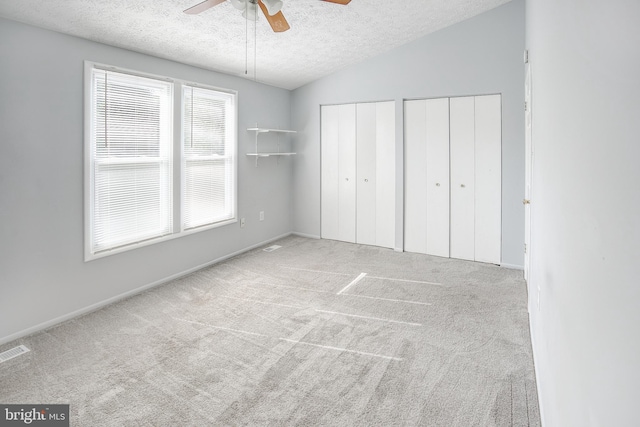 unfurnished bedroom featuring two closets, a textured ceiling, carpet flooring, ceiling fan, and baseboards