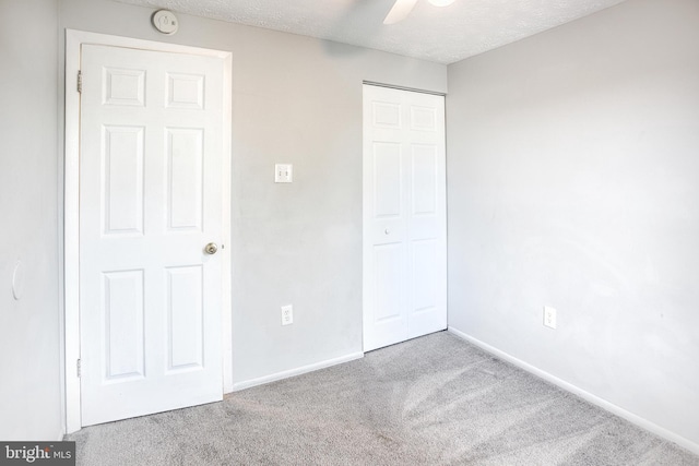 unfurnished bedroom featuring carpet flooring, a closet, baseboards, a textured ceiling, and ceiling fan