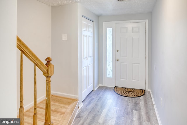 entrance foyer featuring wood finished floors, a textured ceiling, baseboards, and stairs