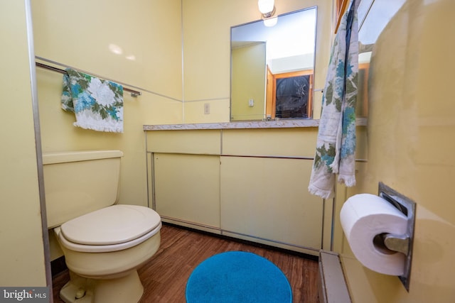 half bath with toilet, wood finished floors, and vanity