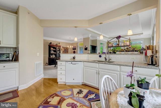 kitchen with white dishwasher, a sink, light wood-type flooring, a tray ceiling, and tasteful backsplash