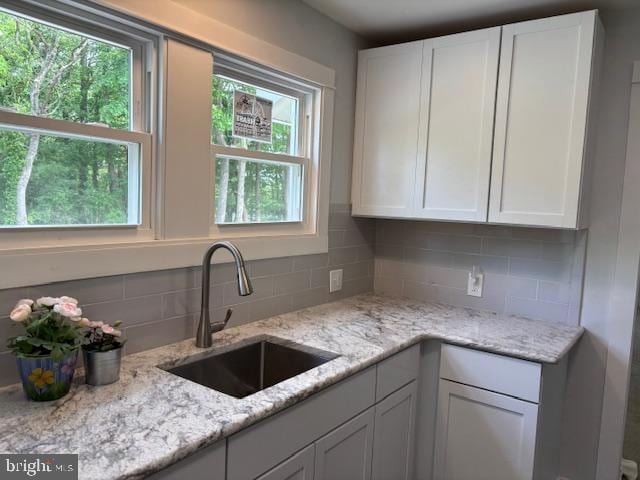 kitchen featuring a sink, decorative backsplash, white cabinets, and light stone countertops