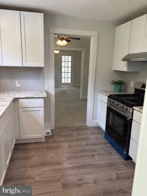 kitchen featuring gas range, under cabinet range hood, white cabinetry, and a ceiling fan