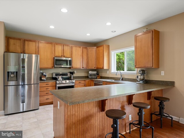 kitchen featuring appliances with stainless steel finishes, recessed lighting, a peninsula, a sink, and a kitchen bar