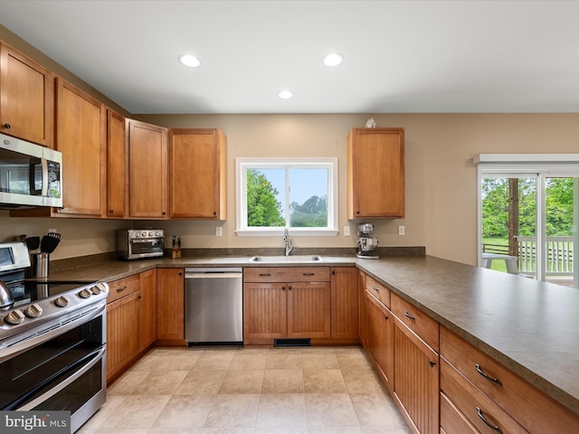 kitchen featuring appliances with stainless steel finishes, a sink, plenty of natural light, dark countertops, and recessed lighting