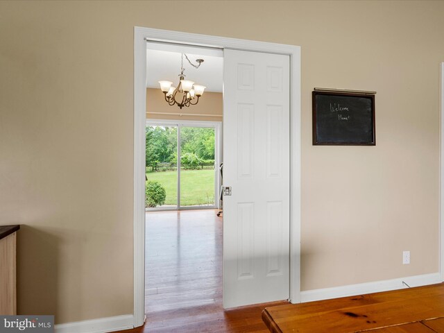 doorway to outside with a chandelier, wood finished floors, and baseboards