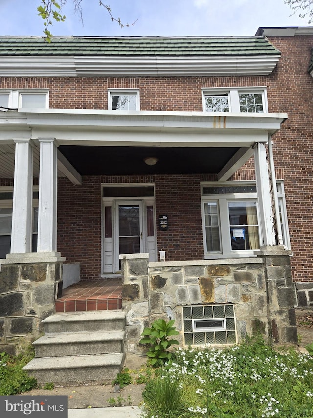 doorway to property with a porch, brick siding, and cooling unit