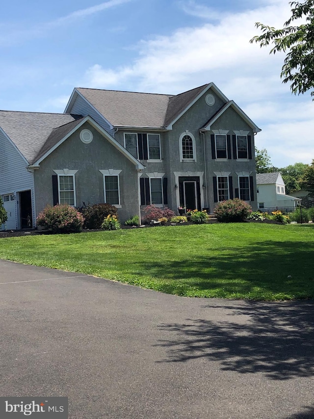 colonial home with stucco siding, a front lawn, and roof with shingles