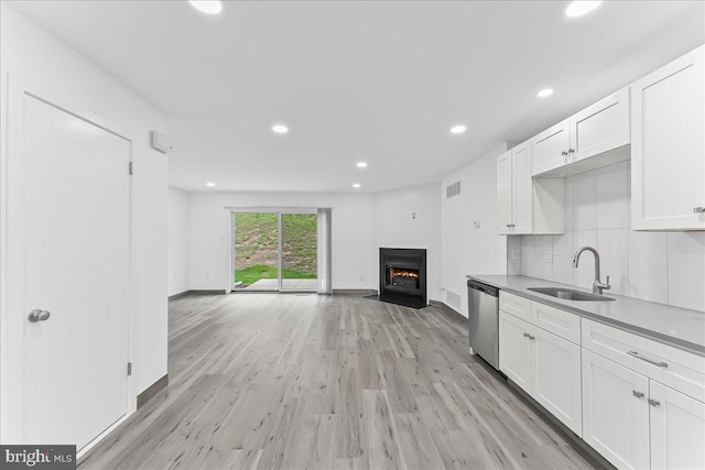 kitchen with a sink, stainless steel dishwasher, light wood-type flooring, white cabinetry, and open floor plan