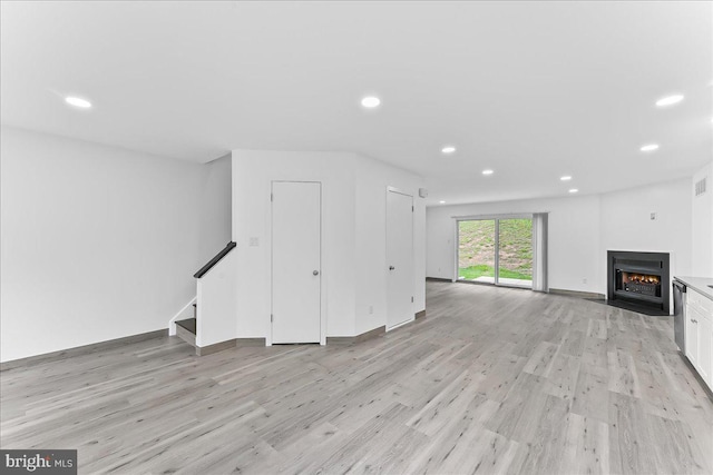 unfurnished living room featuring light wood-type flooring, recessed lighting, a fireplace with flush hearth, stairway, and baseboards