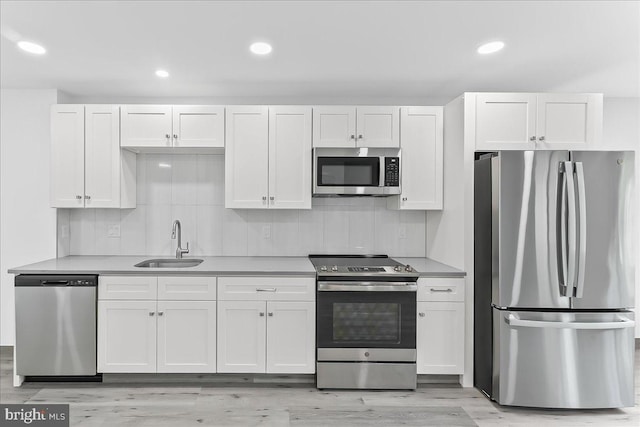 kitchen featuring stainless steel appliances, a sink, white cabinetry, decorative backsplash, and recessed lighting
