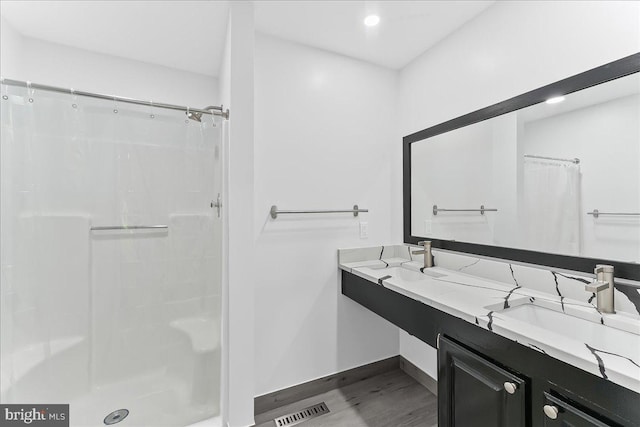 full bath with wood finished floors, a shower with shower curtain, baseboards, double vanity, and recessed lighting