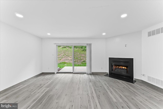 unfurnished living room with a fireplace with flush hearth, wood finished floors, recessed lighting, and baseboards