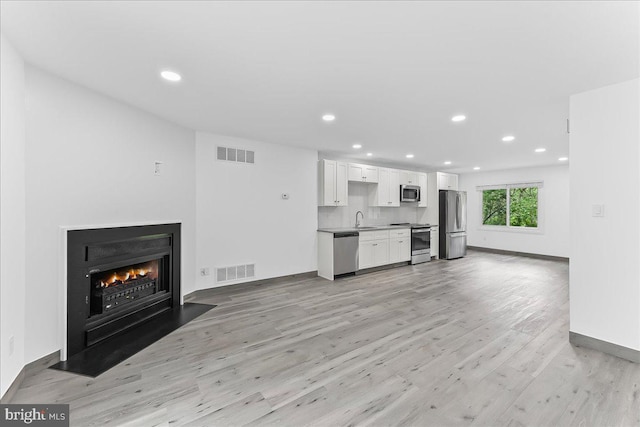 unfurnished living room with a sink, light wood-type flooring, recessed lighting, a fireplace with flush hearth, and baseboards