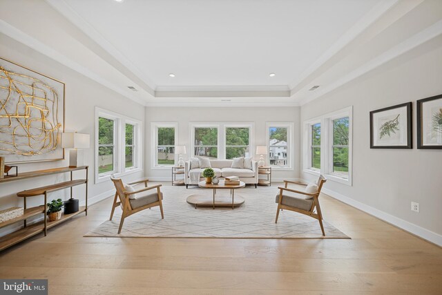 living area with plenty of natural light, a tray ceiling, baseboards, light wood-type flooring, and crown molding