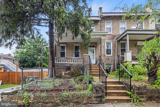 view of property with covered porch, brick siding, and stairway