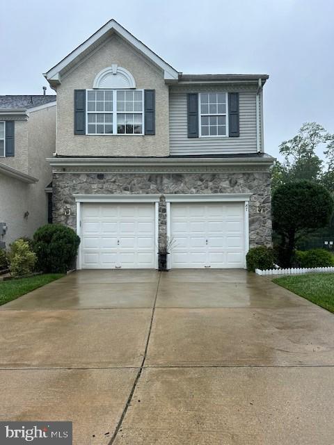 traditional-style home featuring a garage, concrete driveway, and stone siding