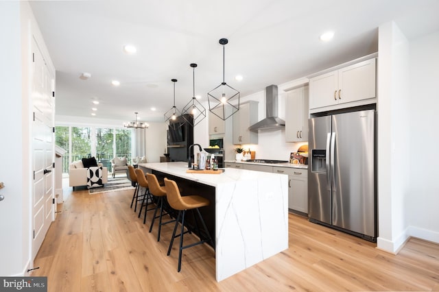 42152 Stone Press Ter, Brambleton, VA 20148 - kitchen featuring appliances with stainless steel finishes, wall chimney exhaust hood, a kitchen bar, a sink, and light wood-type flooring