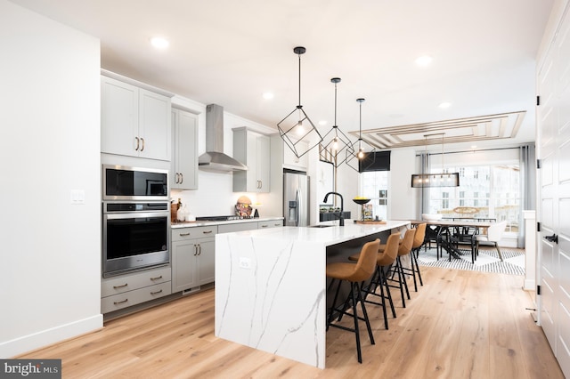 42152 Stone Press Ter, Brambleton, VA 20148 - kitchen featuring stainless steel appliances, wall chimney exhaust hood, gray cabinets, a breakfast bar, and light stone counters