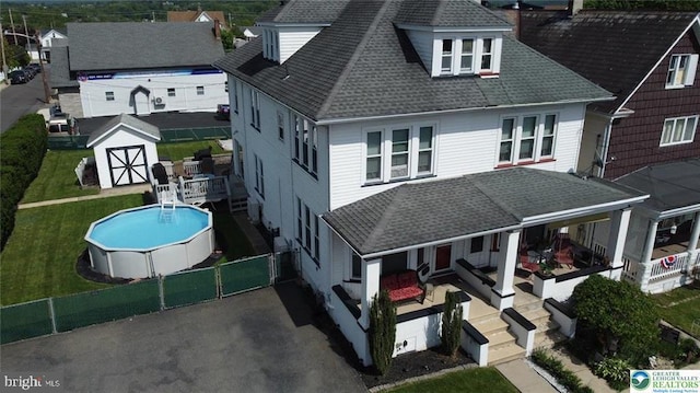 back of property featuring a shed, roof with shingles, an outbuilding, and an outdoor pool