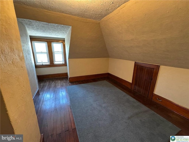 additional living space featuring a textured ceiling, dark wood-type flooring, lofted ceiling, and baseboards