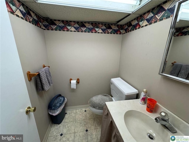 half bathroom with tile patterned flooring, baseboards, toilet, and vanity