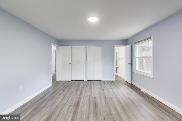 unfurnished bedroom featuring multiple closets, wood finished floors, baseboards, and connected bathroom